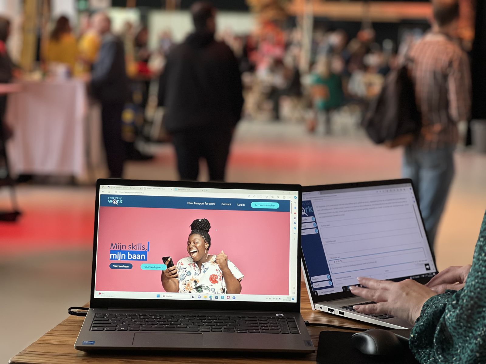 Laptop met de website van Passport for Work op een tafel tijdens het vacaturecafé, met bezoekers op de achtergrond