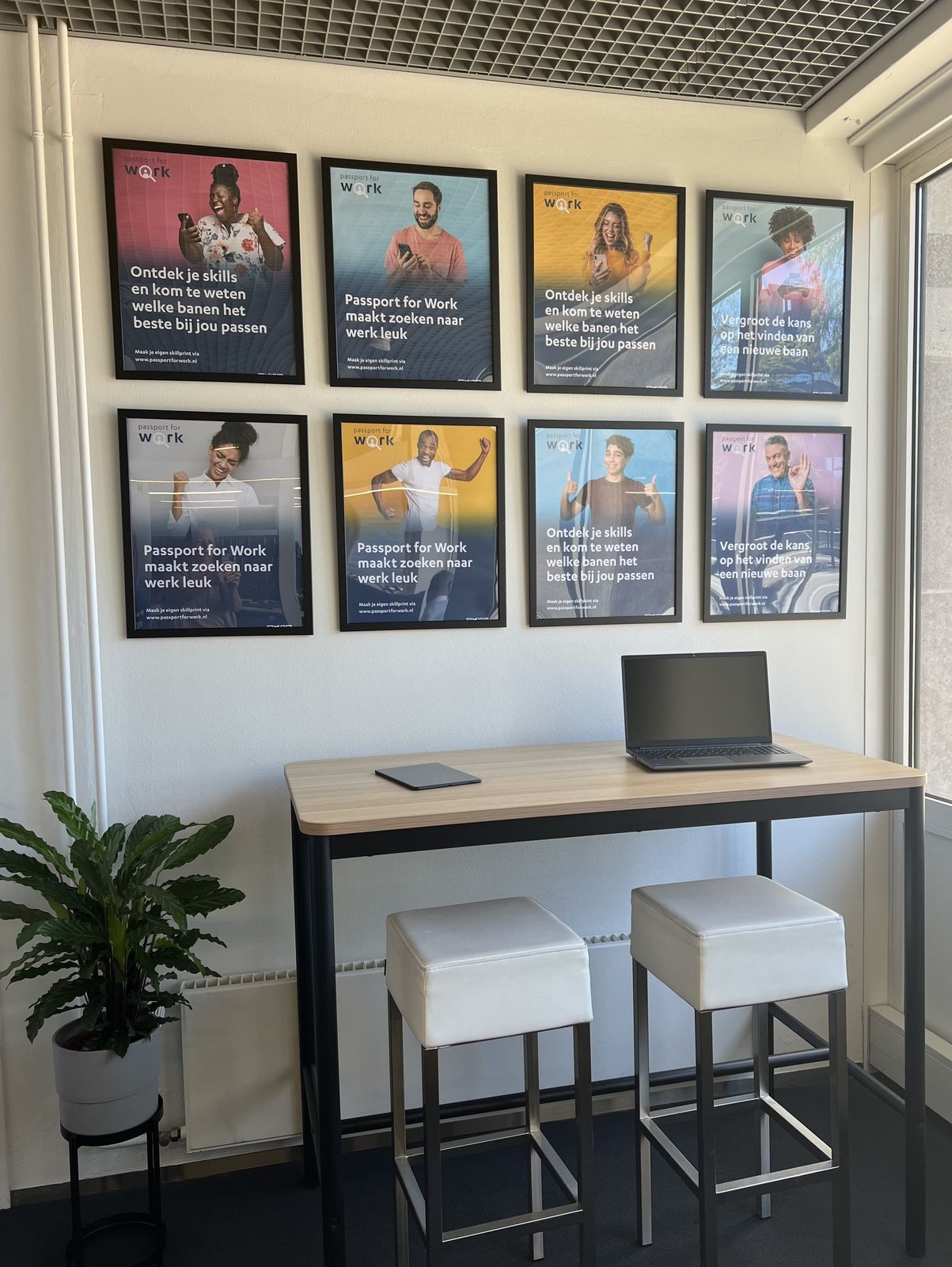De skillsroom in Eindhoven: een statafel met laptop en twee krukken onder acht posters van Passport for Work