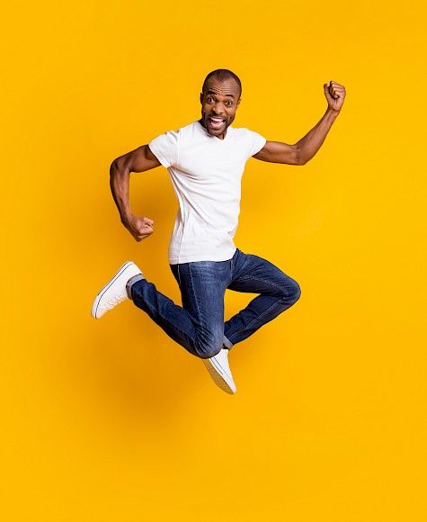 Blije man in een wit T-shirt die een sprong maakt voor een gele achtergrond