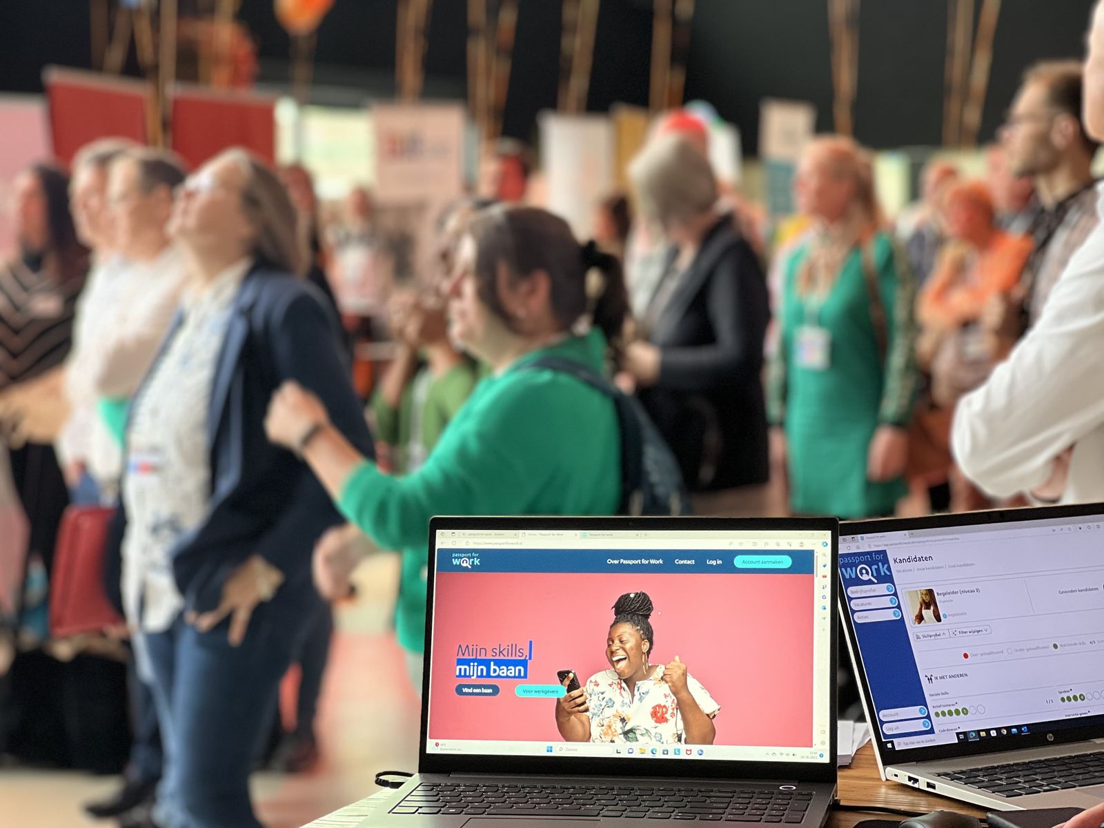 Bezoekers van de banenmarkt, met op de voorgrond twee laptops met de website en het platform van Passport for Work